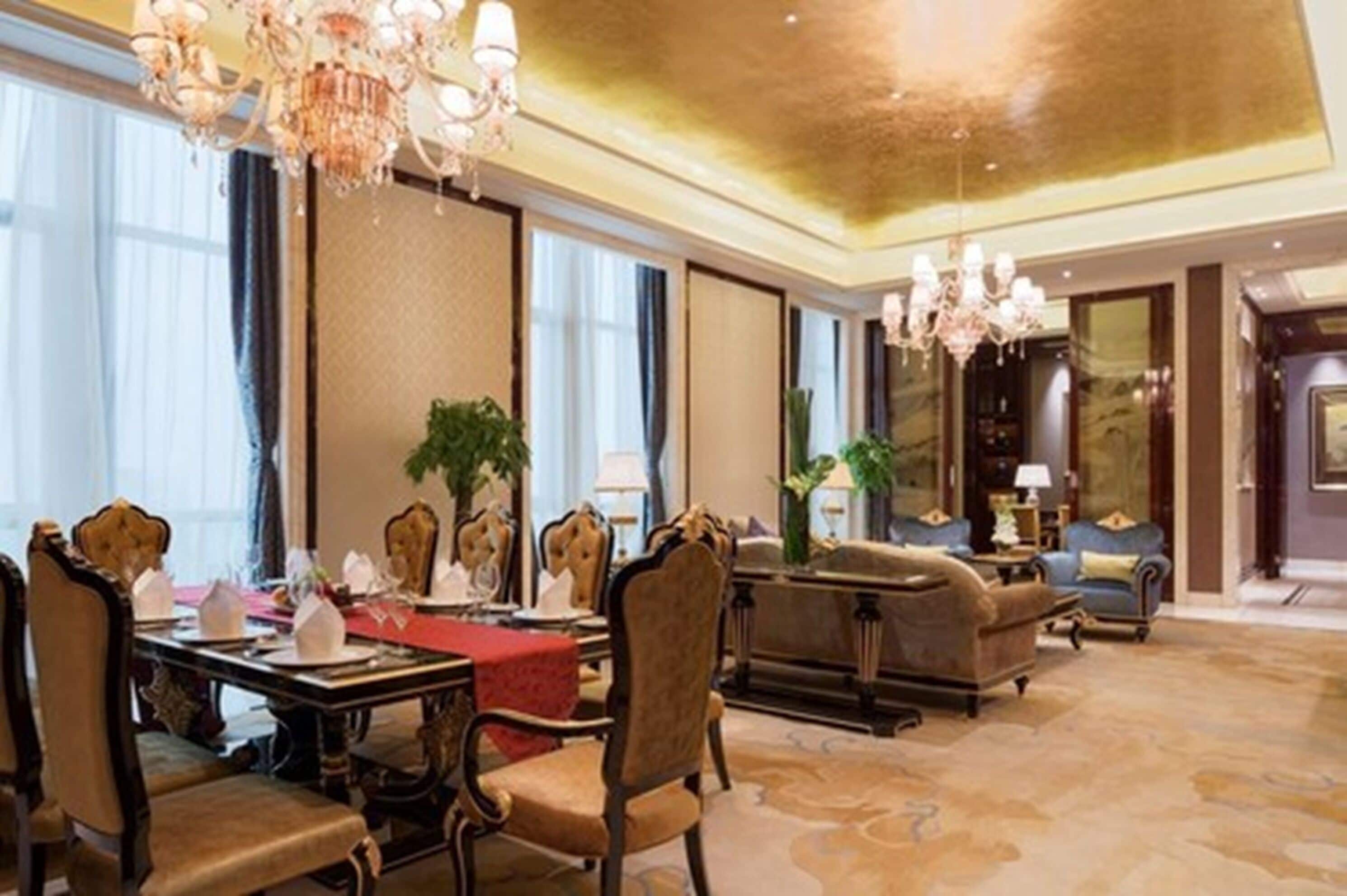 A luxurious hotel lobby with a dining area, elegant chandeliers, plush seating, and large windows.