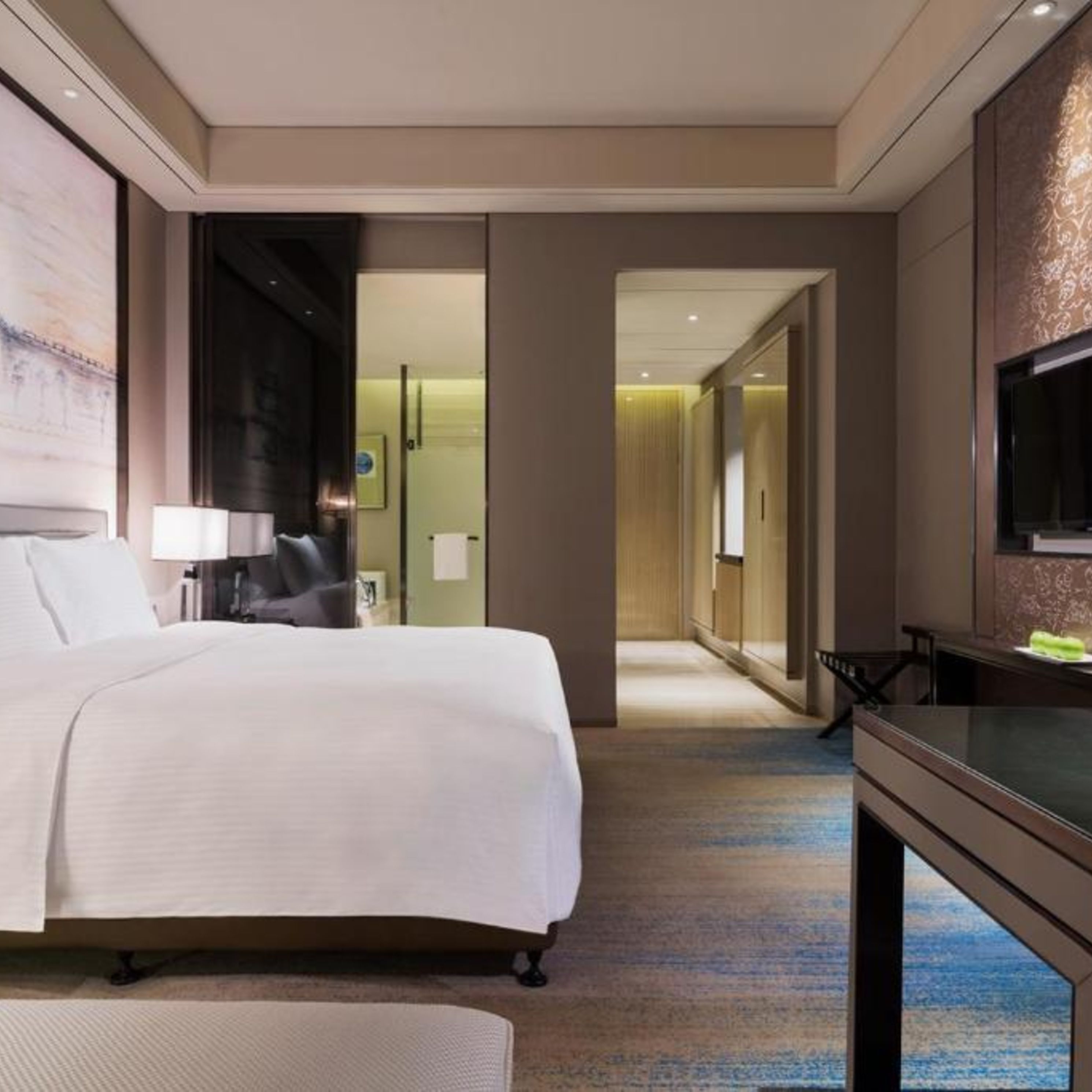 Habitación de hotel con una cama grande, un escritorio, televisión y un baño visible a través de una puerta abierta.