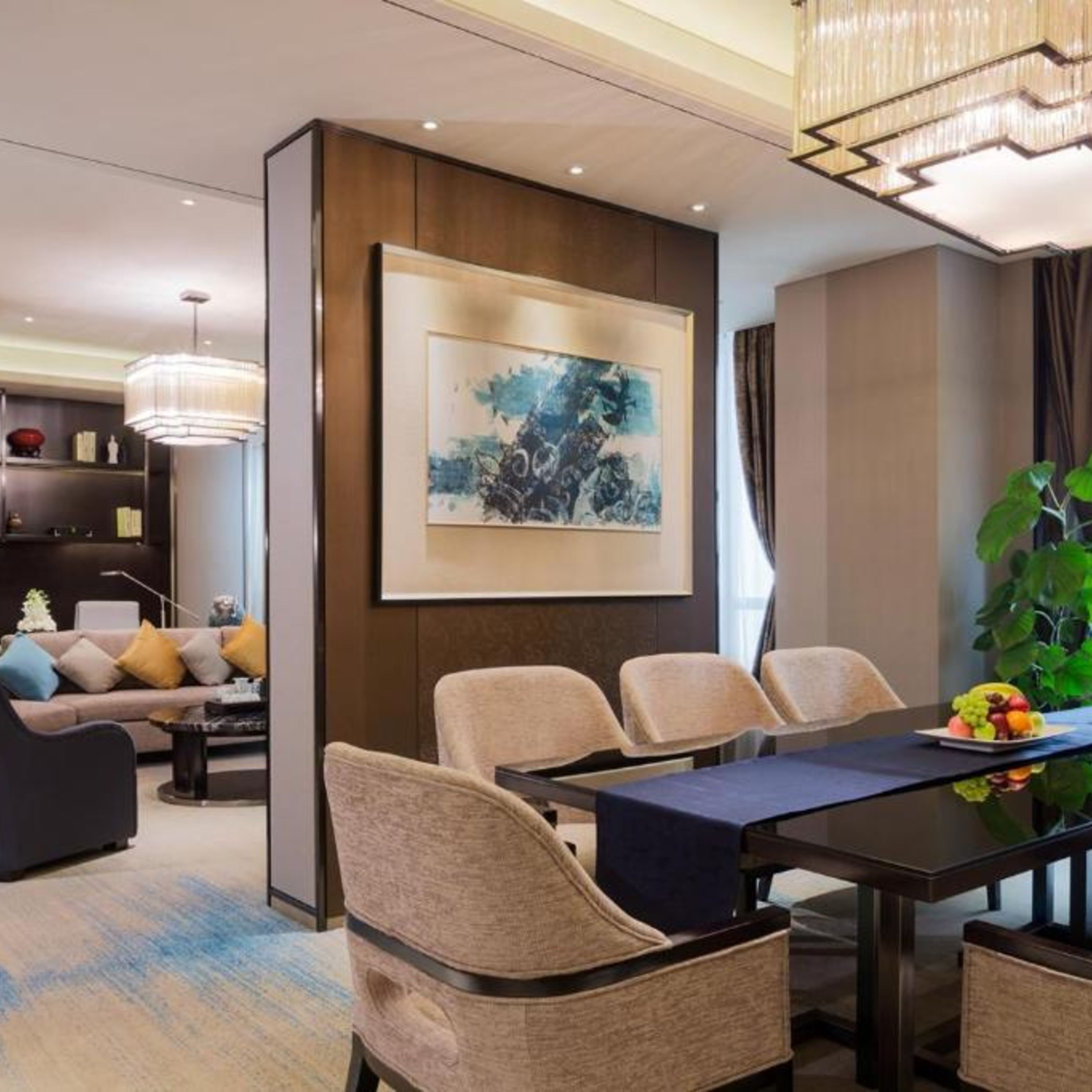 A modern hotel room with a dining area, a large painting on the wall, and a plant on the table.