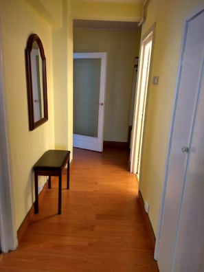 Un couloir avec un plancher en bois, un banc, une porte et un miroir accroché au mur.