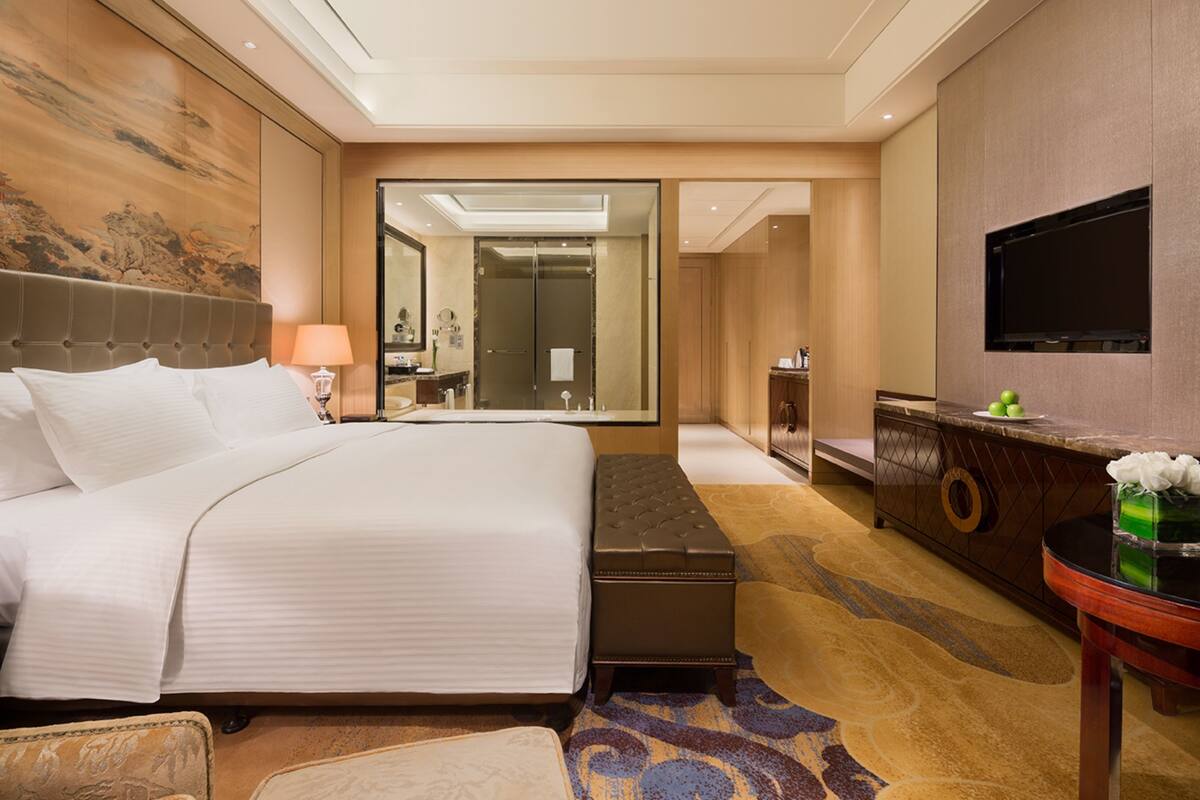A hotel room with a large bed, a sitting area, a mirror, a television, and a small table.