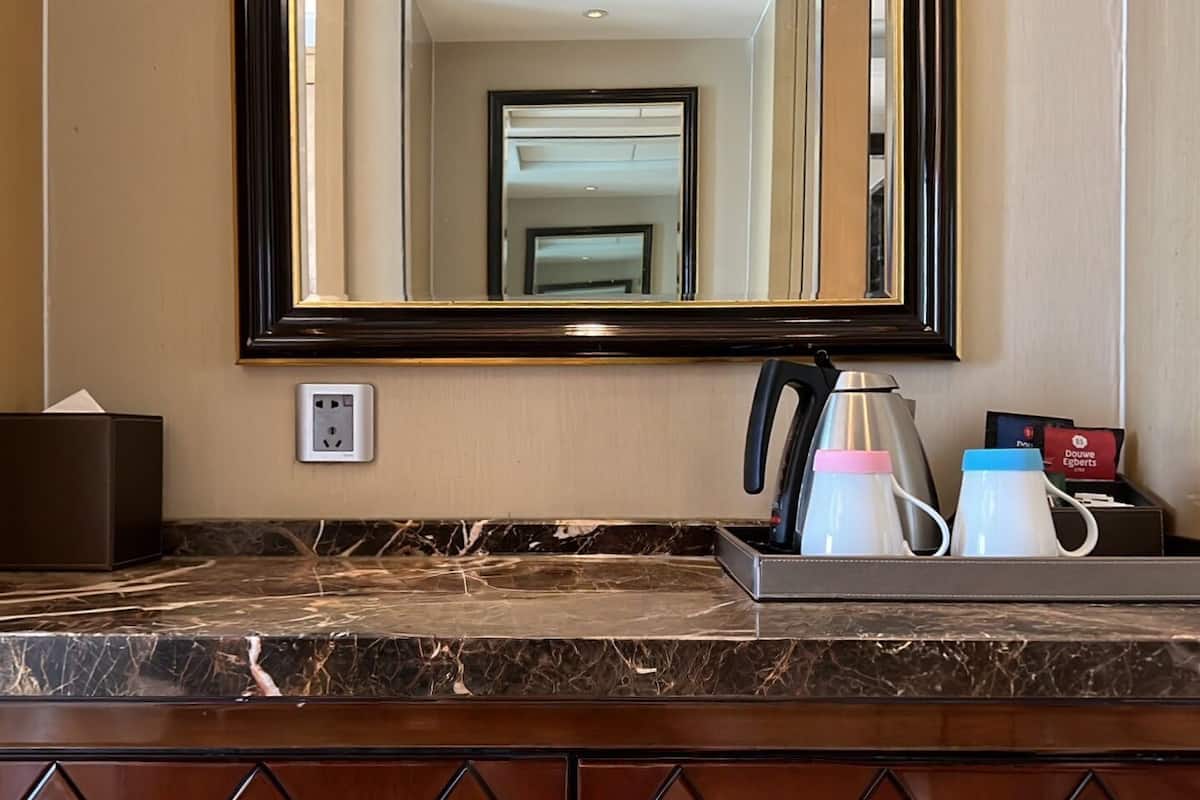 A hotel bathroom with a marble countertop, a large mirror, a coffee maker, and toiletries.