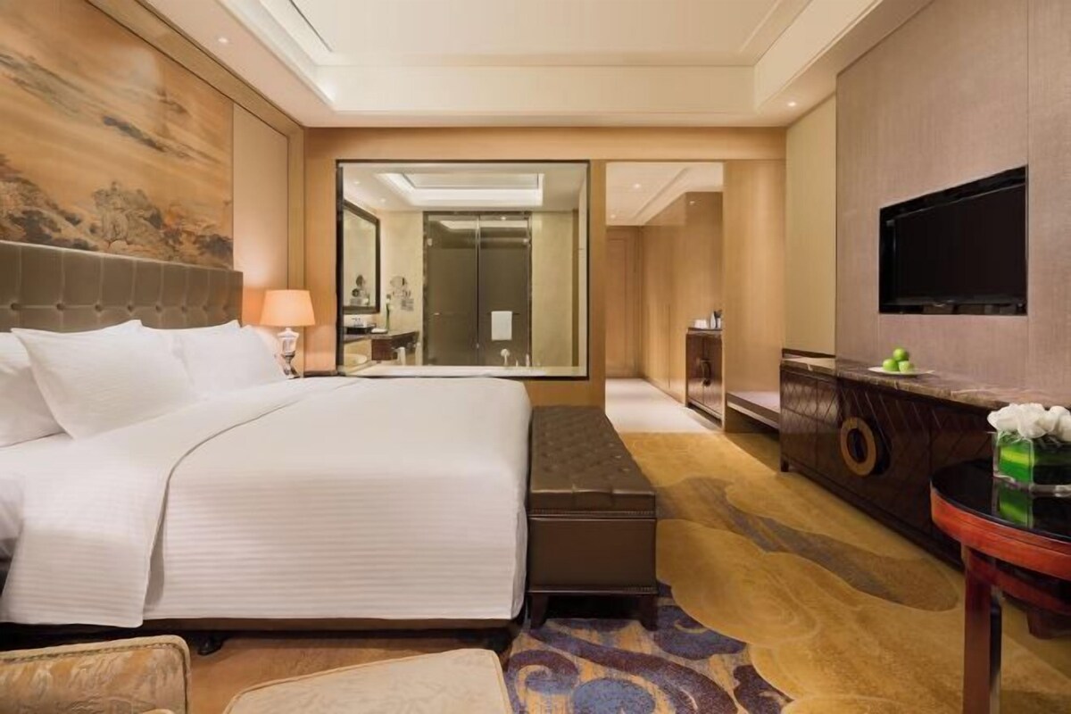 Una habitación de hotel con una cama grande, una mesita de noche, un espejo, un televisor y un armario.