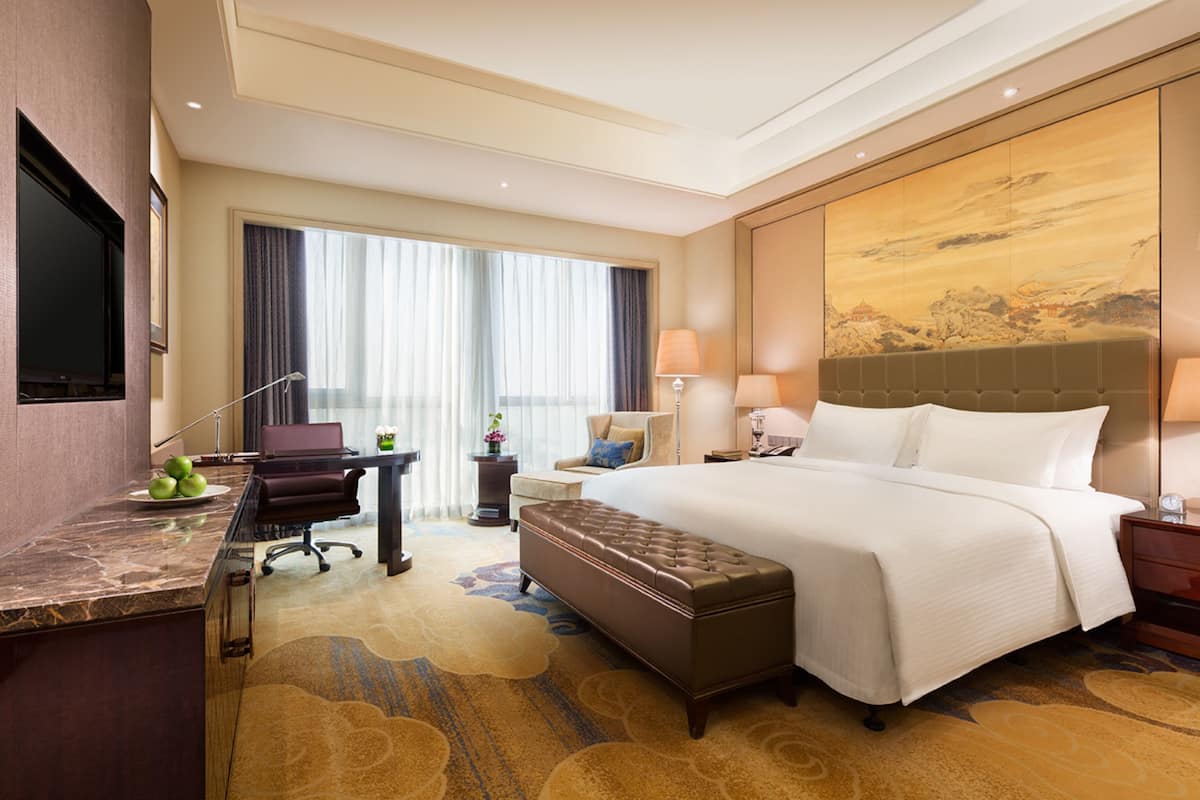 A hotel room with a large bed, a desk with a computer, a seating area, and a TV.