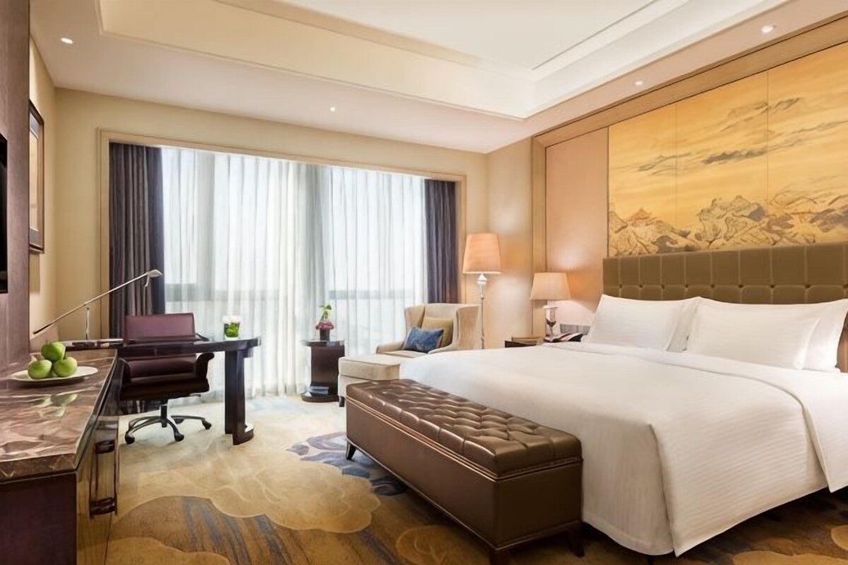 Habitación de hotel con una cama grande, un escritorio, una silla, una mesita y una ventana con cortinas.