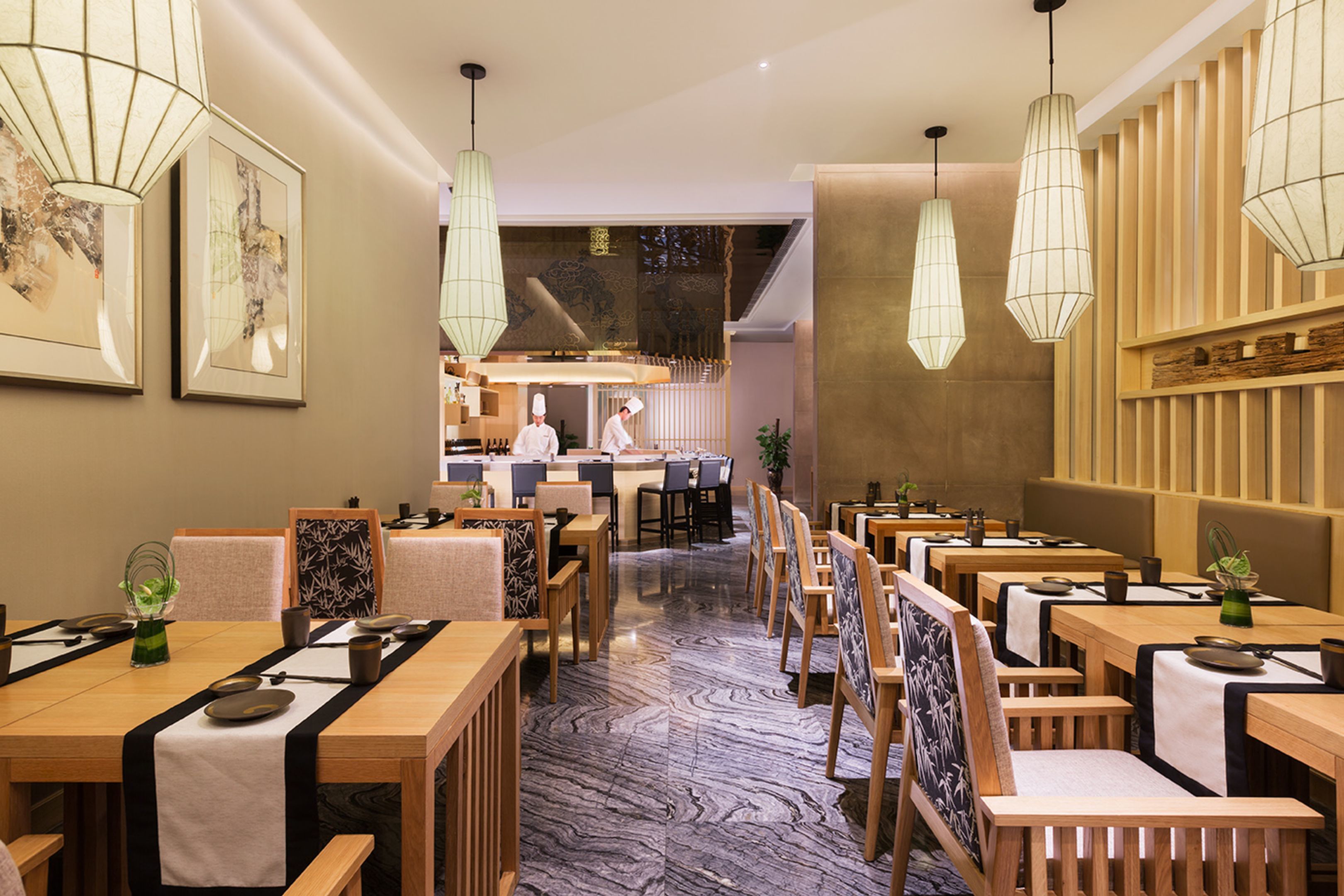 A restaurant with wooden tables and chairs, hanging light fixtures, and framed artwork on the walls.