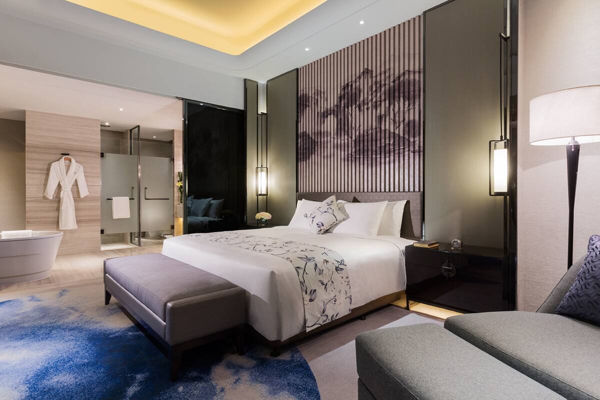 Habitación de hotel moderna con una cama grande, un área de estar, una bañera y una obra de arte colgada en la pared.