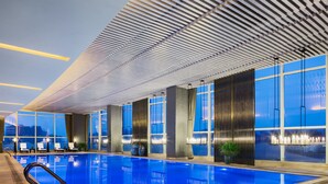 An indoor swimming pool with a modern design, large windows, and a poolside area with lounge chairs and a small table. - Wanda Realm Wuhu (Wuhu)