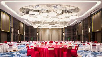 A banquet hall with round tables, red and white tablecloths, and a large chandelier.