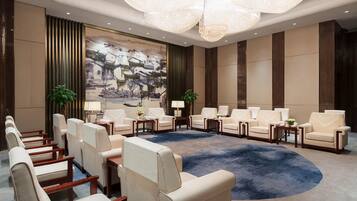A spacious conference room with a large round table, multiple chairs, and a large painting on the wall.