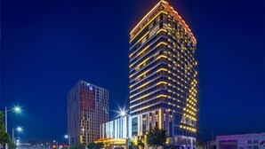 Un hotel moderno de gran altura con varias plantas, ventanas iluminadas y una entrada destacada con toldo.