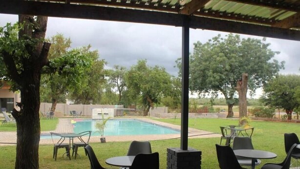 Um pátio externo com piscina, cercado por árvores e uma área coberta com mesas e cadeiras.