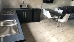 Cozinha compacta com micro-ondas, fogão e pia. Há uma área de refeições com mesa e cadeiras.