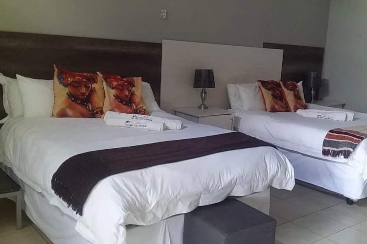 Two single beds with white linens and decorative pillows, a bedside table with a lamp, and a bench at the foot of the beds.