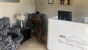 A reception area with a reception desk labeled "The Dam Vista Retreat," a patterned sofa, a vase with flowers, and a clock on the wall.