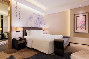 A hotel room with a large bed, two bedside tables, a nightstand, a sofa, and a wall with a floral mural.