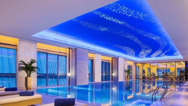 An indoor swimming pool with lounge chairs and a ceiling with a light display. - Wanda Realm Jining (Jining)