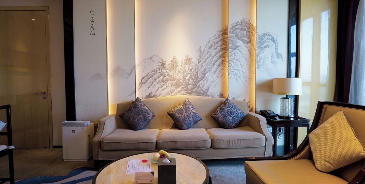 A hotel room with a sofa, a coffee table, a lamp, and a small table with a phone and a lamp.