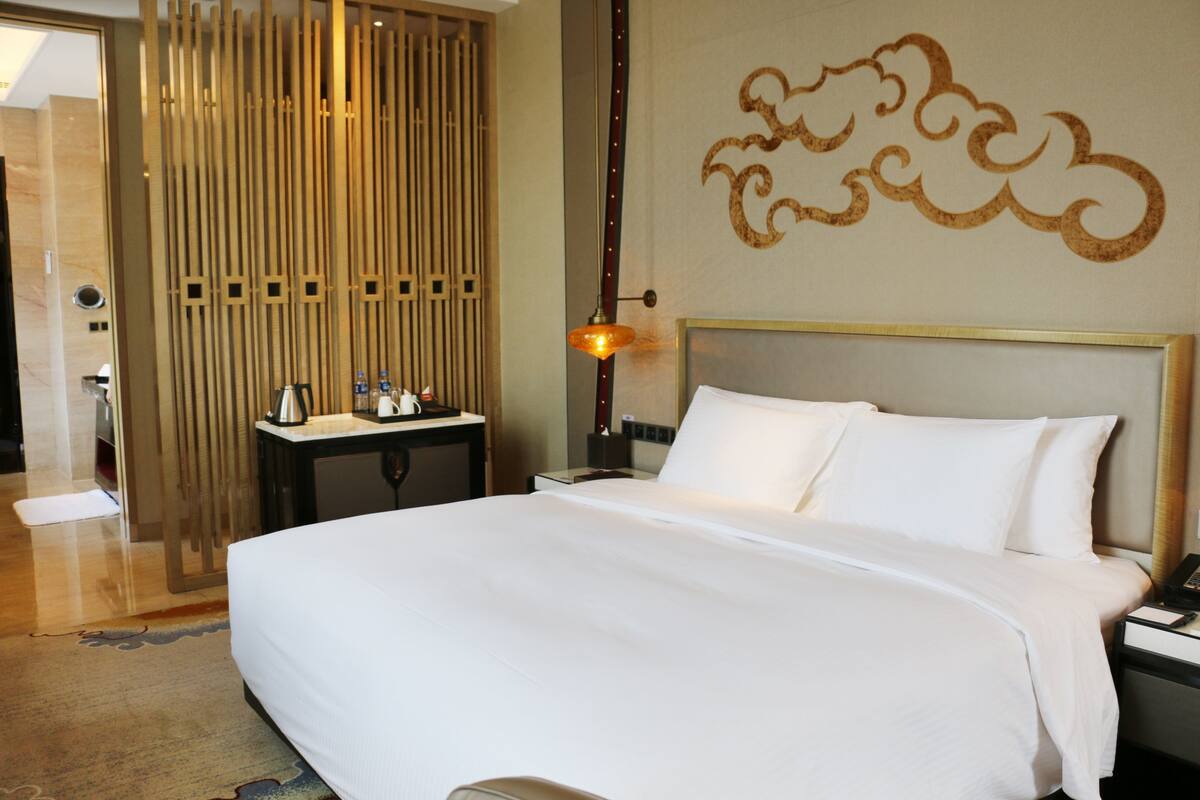 Habitación de hotel con una cama grande, una mesita de noche con lámpara, una separador de madera y un diseño decorativo en la pared.