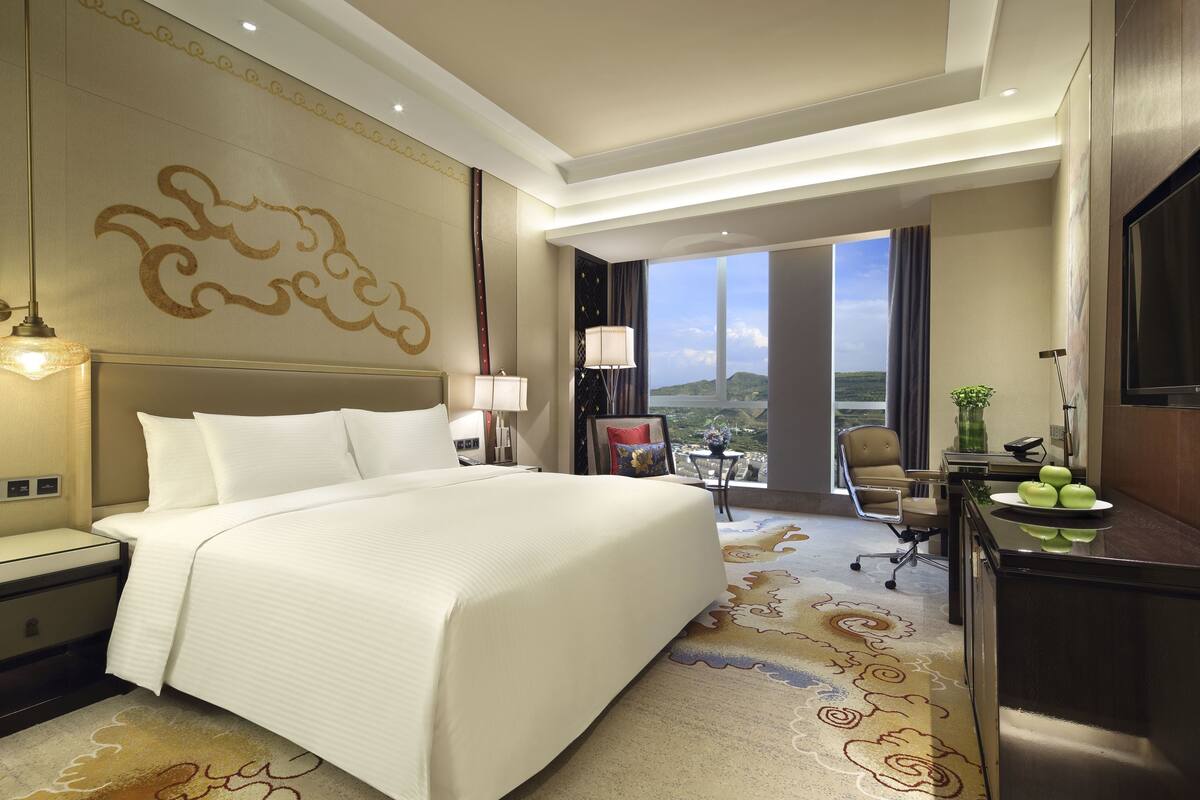 Habitación de hotel con una cama grande, un escritorio con silla, televisor y vistas al exterior.