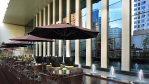 A modern outdoor dining area with tables and chairs, large umbrellas, and a water feature. - Wanda Vista Xining (Xining)