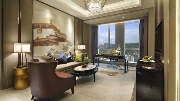A spacious living room with a large window, a chandelier, a sofa, a coffee table, and a TV.