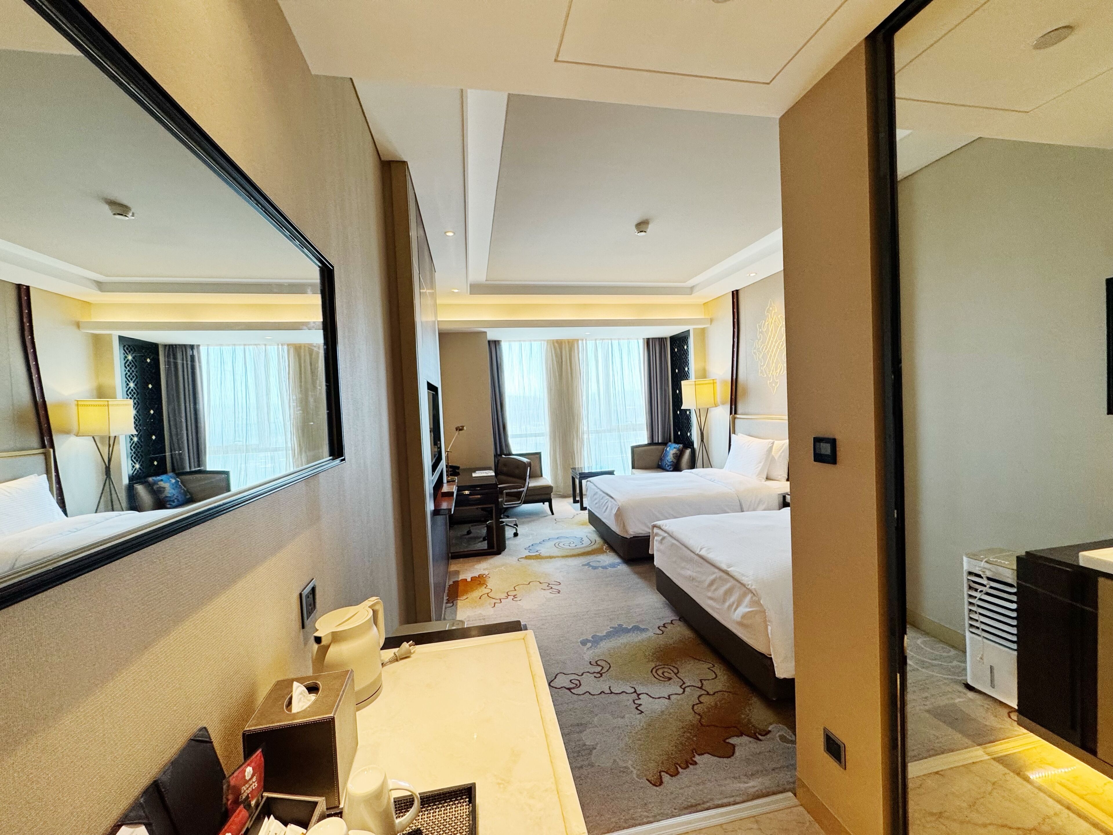 A hotel room with two beds, a desk, a mirror, a coffee maker, and a TV.