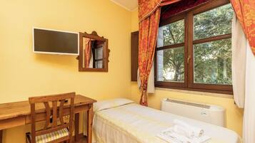 A small, tidy room with a wooden desk, a single bed, a radiator, and a window with curtains.