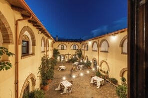An outdoor courtyard with multiple tables and chairs, surrounded by arches and potted plants. - Hotel Funtana Noa (Villanovaforru)