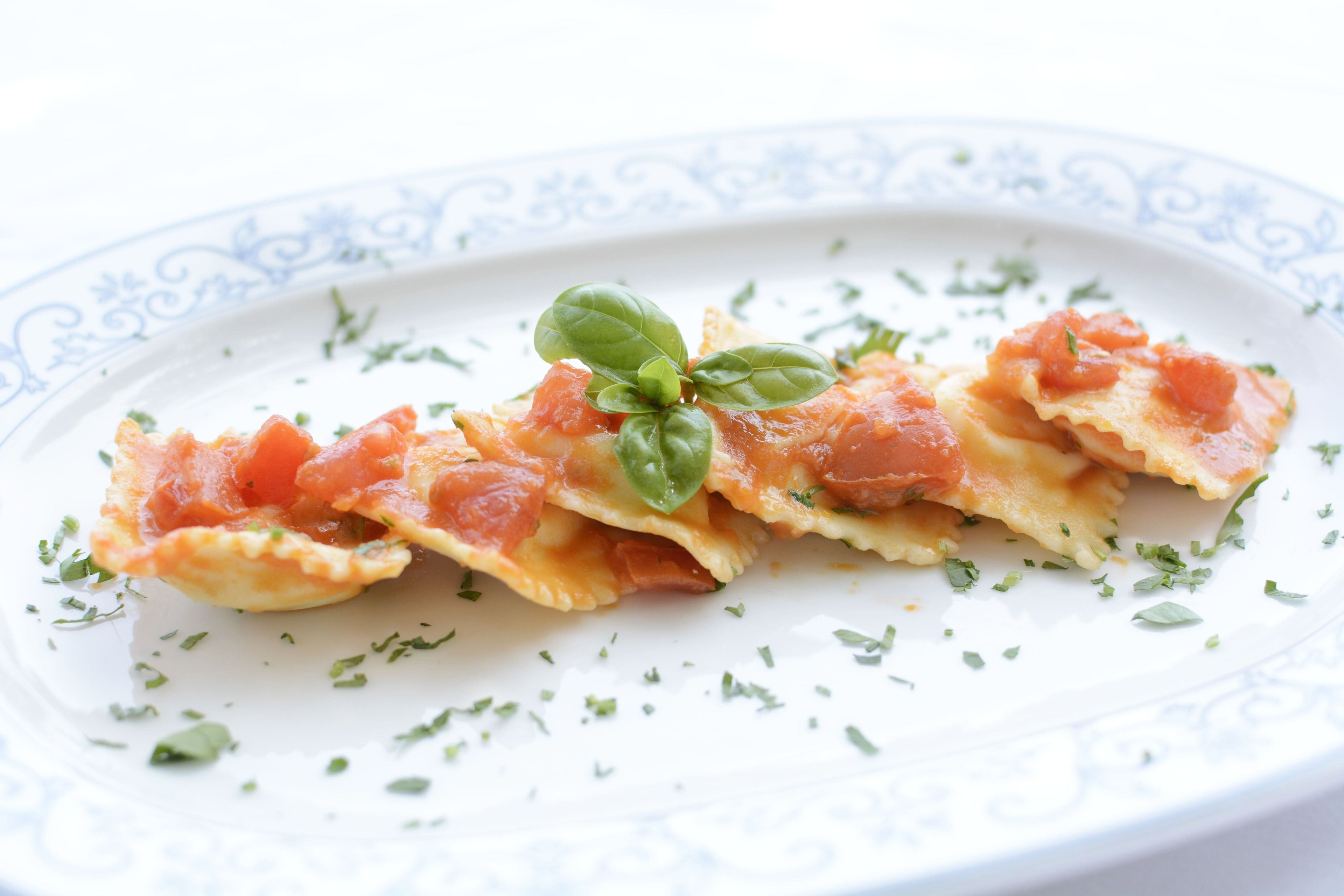 Een bord ravioli met tomatensaus en basilicum.