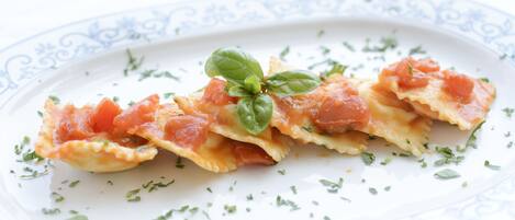 Une assiette de raviolis nappés de sauce tomate et décorée de feuilles de basilic.