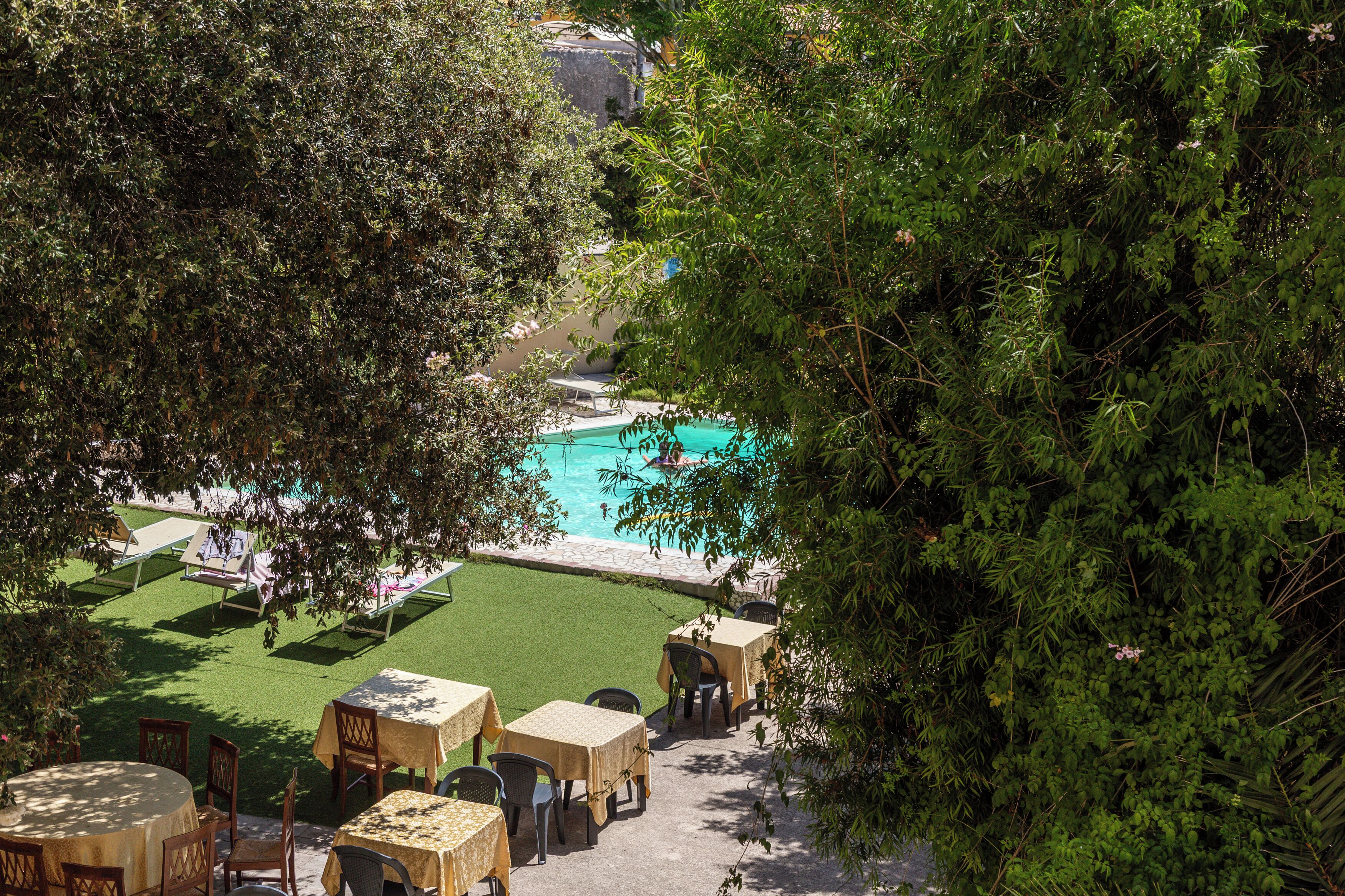 Un área de piscina con mesas y sillas, rodeada de vegetación.