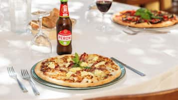 Een eettafel met pizza, een fles Peroni bier, wijnglazen en bestek.