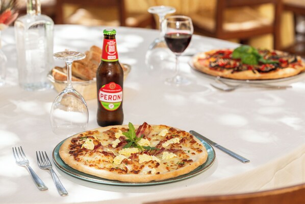 A dining table with a pizza, a bottle of Peroni beer, wine glasses, and cutlery. - Hotel Funtana Noa (Villanovaforru)