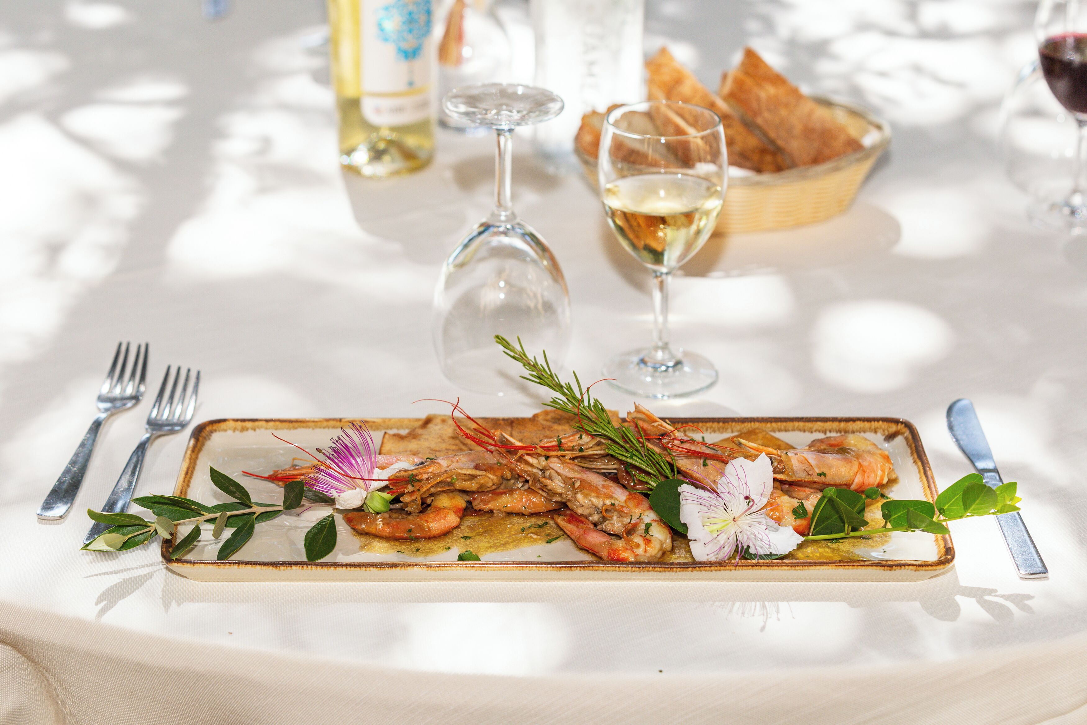 En rätt med skaldjur, tillagad med räkor och garnerad med örter och blommor, serverad på en rektangulär tallrik.