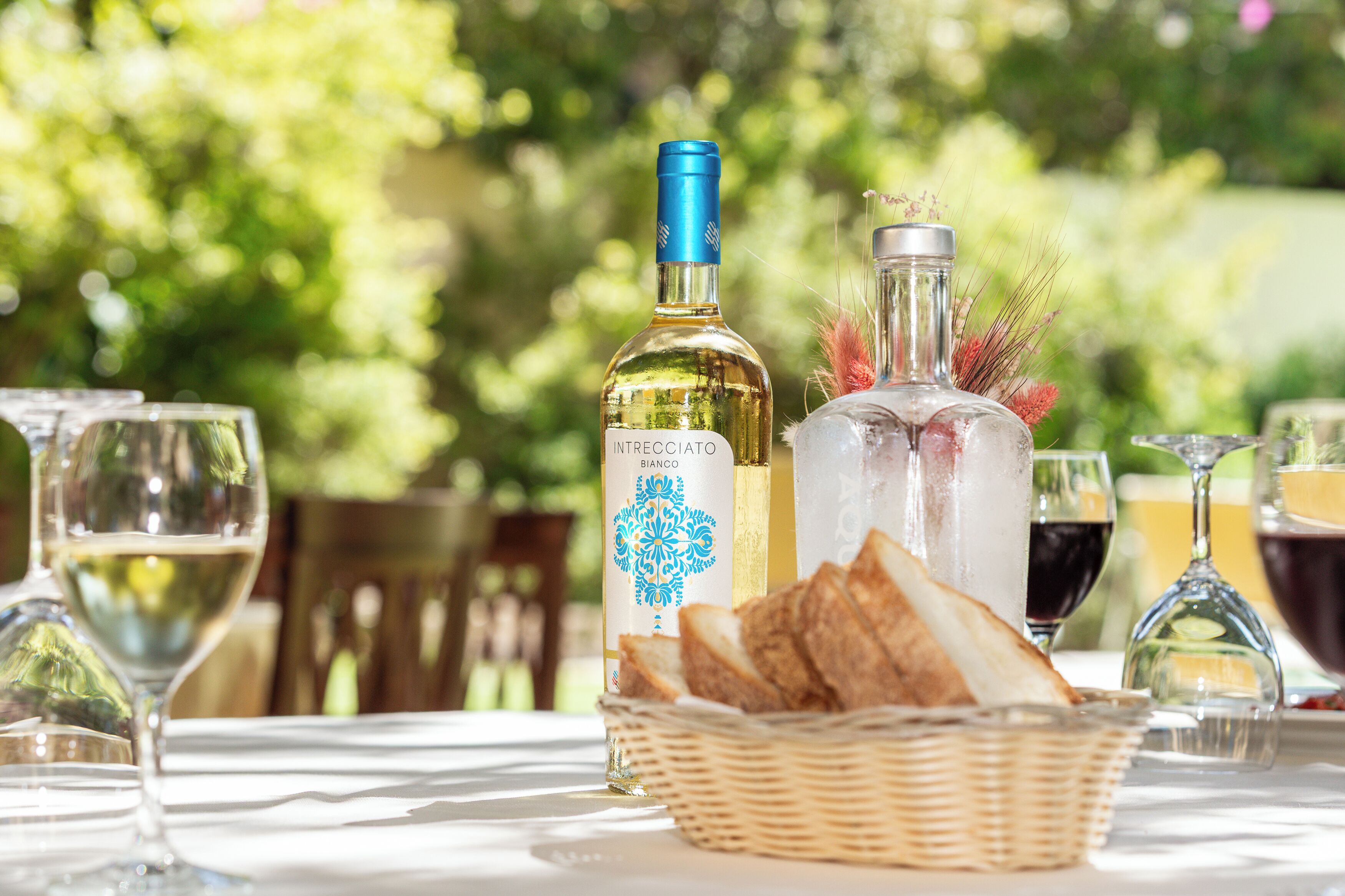 Une table dressée avec des verres à vin, des bouteilles et un panier de pain.