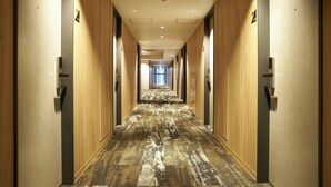 Un largo y estrecho pasillo de hotel con paneles de madera, alfombra estampada e iluminación empotrada en el techo.