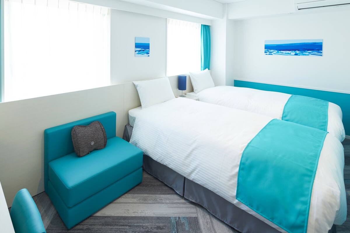 A modern hotel room with a large bed, a small sofa, and a window with a view of the sea.
