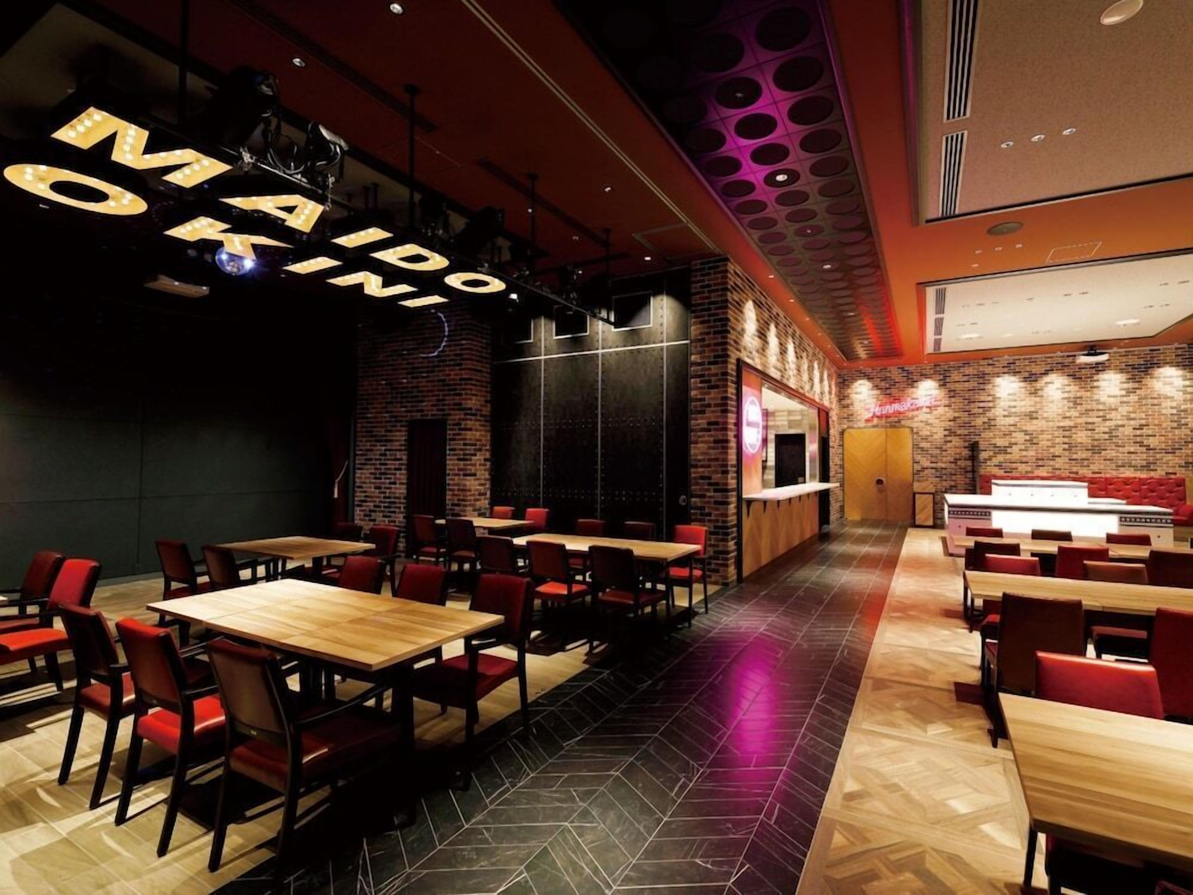A restaurant interior with multiple dining tables and chairs, a brick wall, and a ceiling with circular light fixtures.