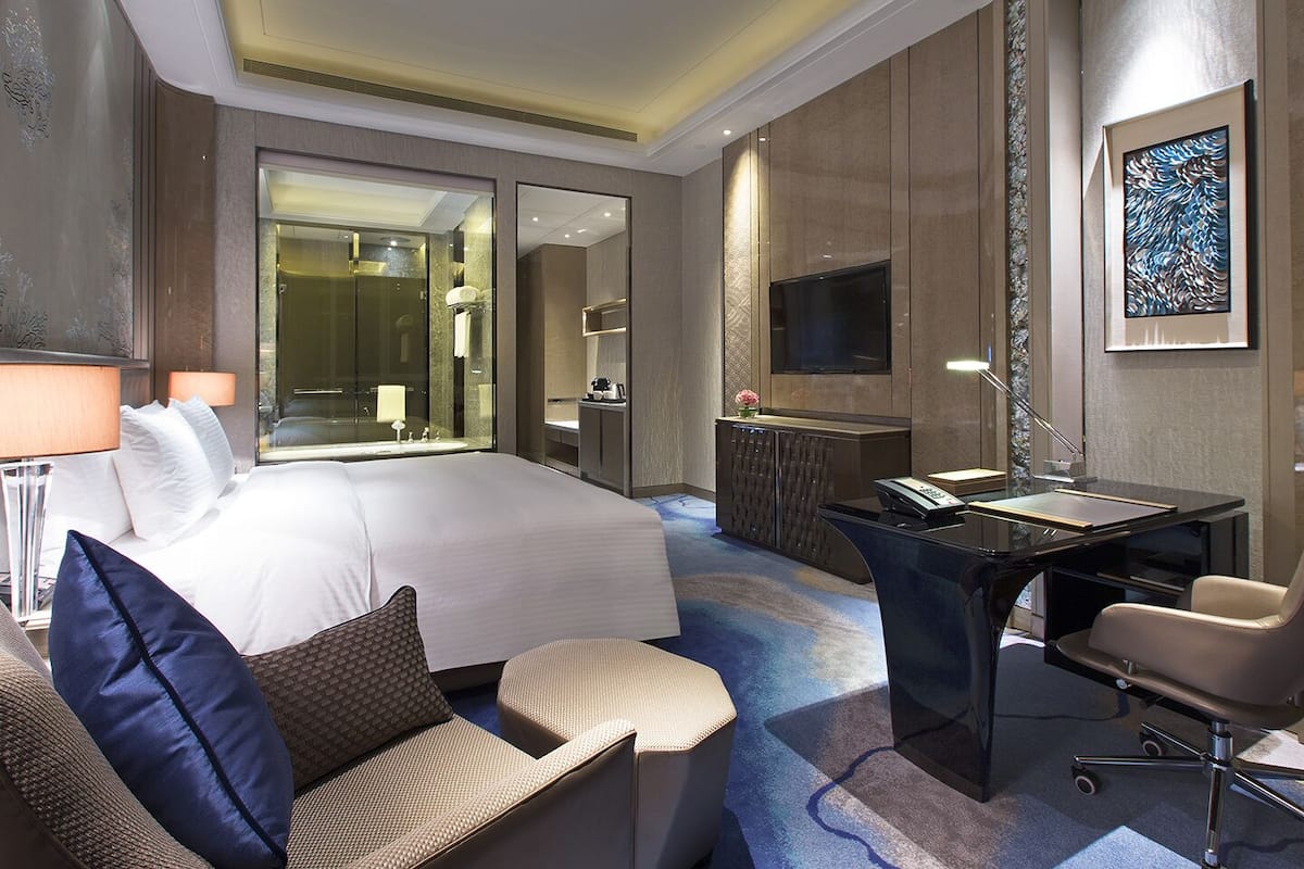 A hotel room with a large bed, a desk, a chair, a TV, and a bathroom.
