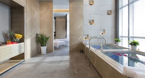 A modern bathroom with a large bathtub, a shower area, and a vanity with a mirror. There are potted plants and flowers on the vanity, and a window with blinds on the right side. - Pullman Yantai Center (Yantai)