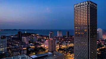 A high-rise hotel with a modern glass facade, surrounded by a cityscape with various buildings and a body of water in the background.