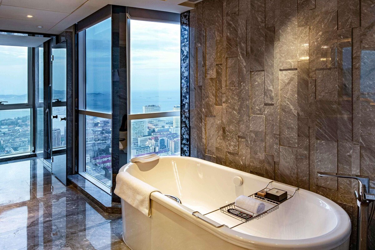 A modern bathroom with a freestanding bathtub, a glass-enclosed shower, and a view of a cityscape.