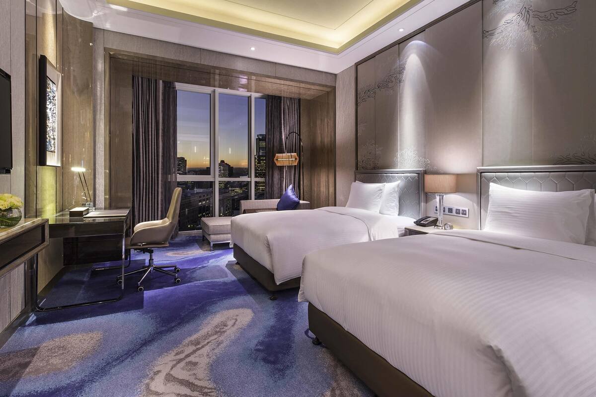 A hotel room with a city view, two beds, a desk, and a chair.