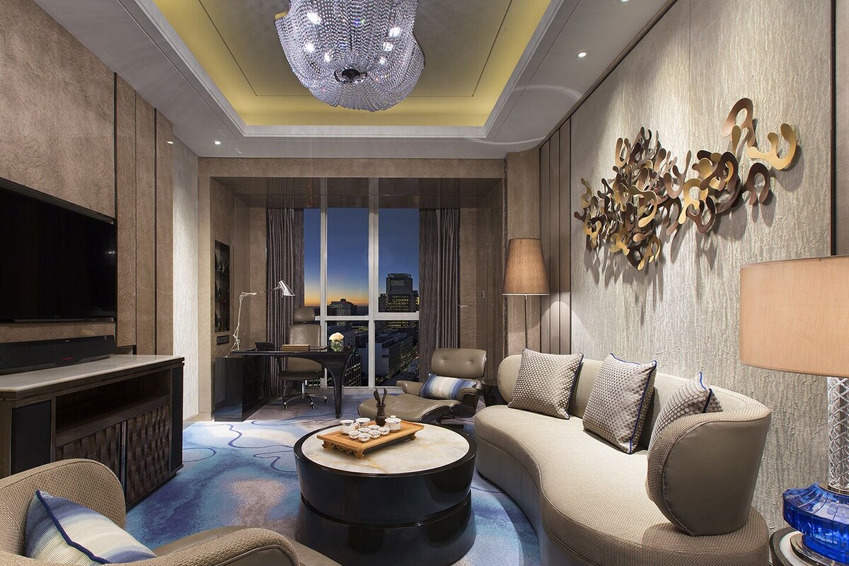 A modern living room with a large flat-screen TV, comfortable seating, a round coffee table, and a city view through large windows.