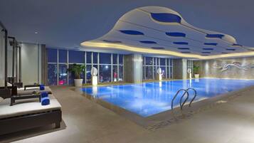 Una piscina interior moderna con vista a la ciudad, un área de descanso con asientos y un diseño de techo singular.
