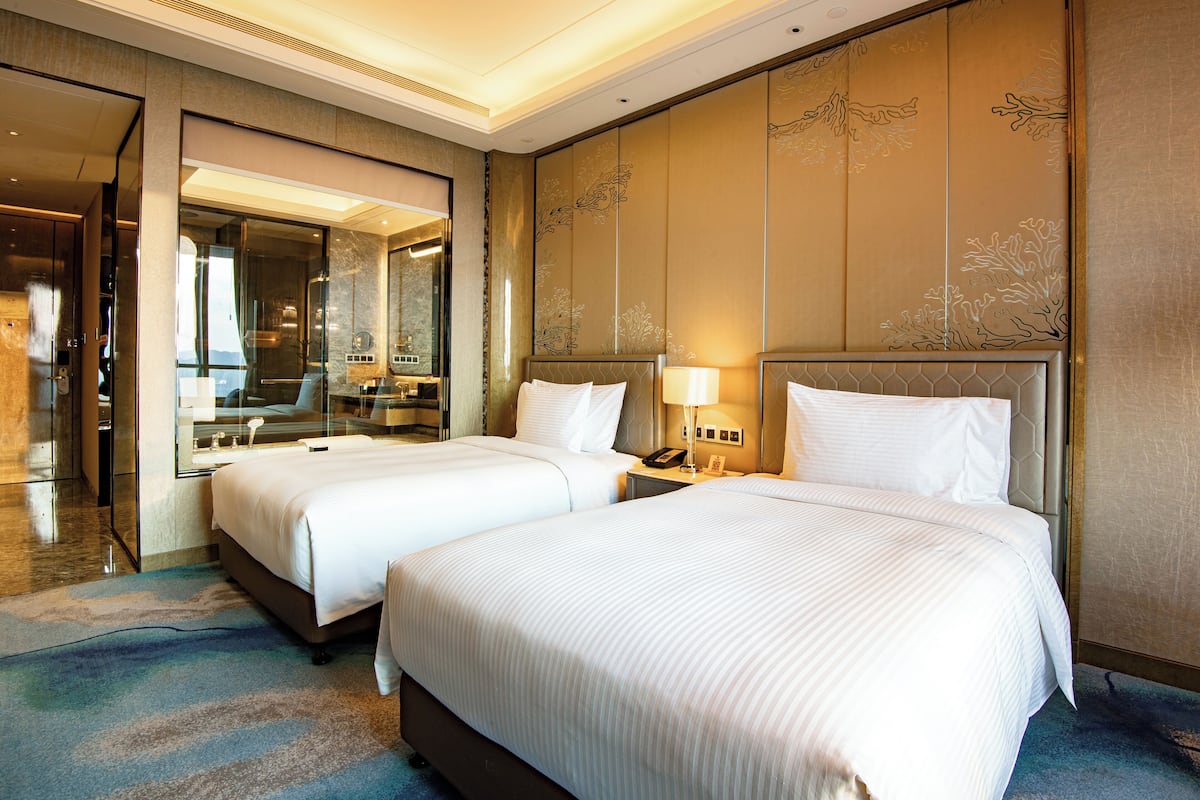 A hotel room with two beds, a large mirror, and a nightstand with a lamp.