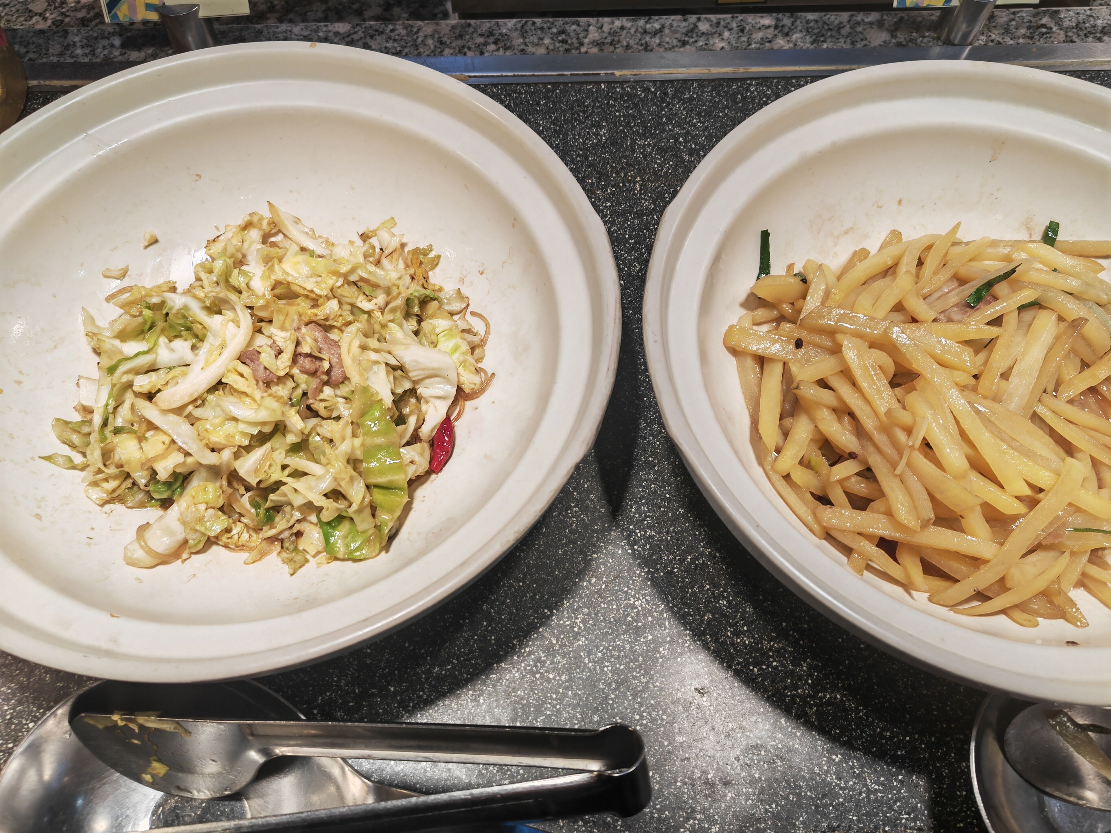 Two white plates on a granite countertop, one with a vegetable stir-fry and the other with French fries.