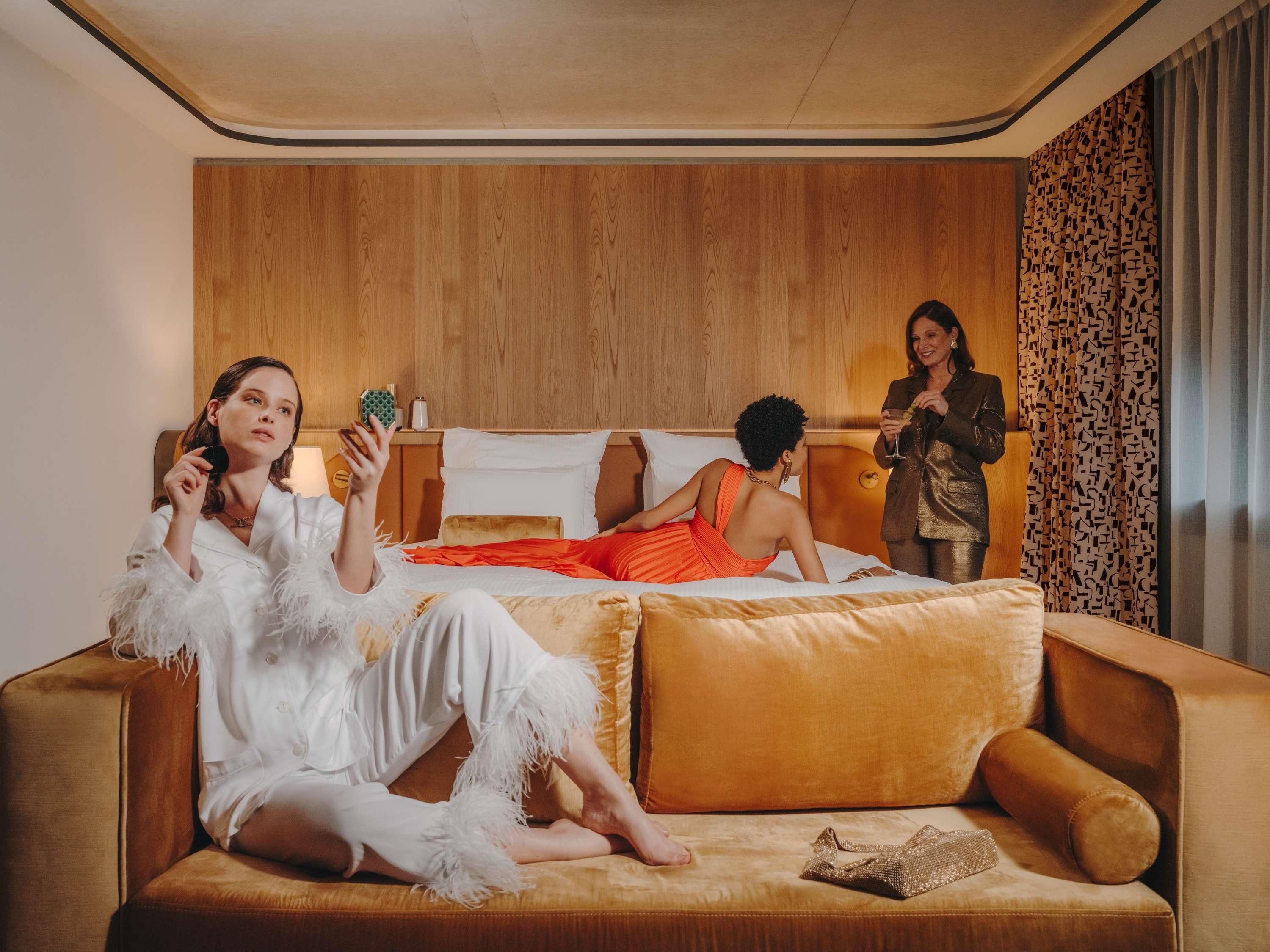 A modern hotel room with a large bed, a sofa, and a wooden headboard.