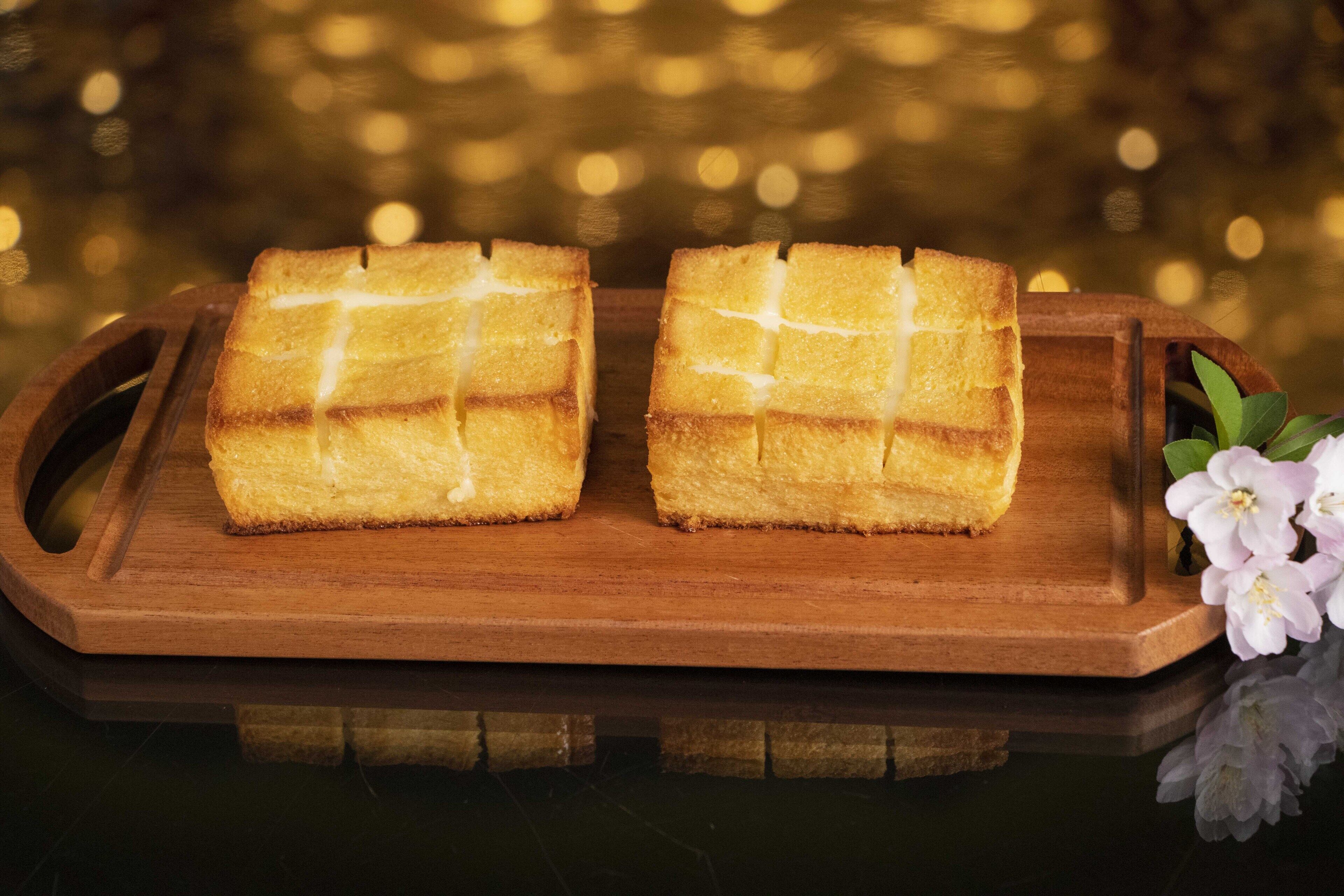 Dois bolos quadrados sobre uma bandeja de madeira com fundo dourado desfocado.